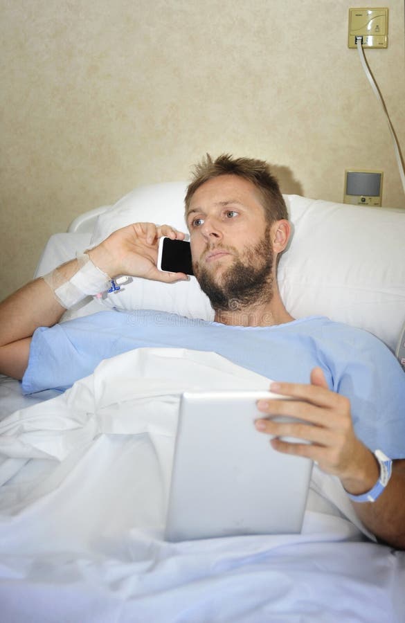 Business man in hospital room lying in bed sick and injured working with mobile phone and digital pad