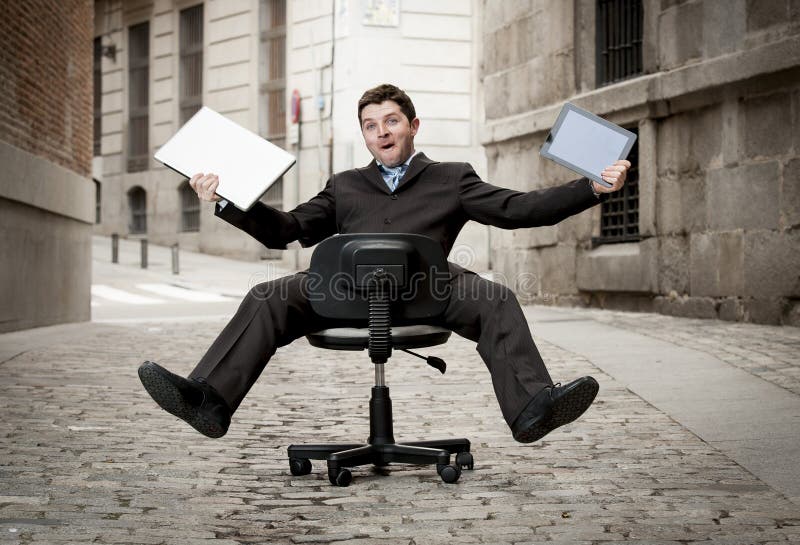 Business man rolling downhill on chair with computer and tablet royalty free stock image