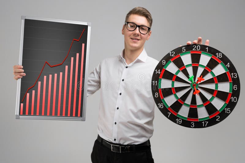 Young Man In Glasses Holding A Board With Increasing Statistics And Darts Isolated On White Background