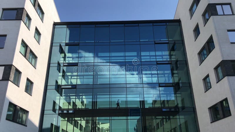 Business man in silhouette walking through a glass hallway in modern office building with reflections of blue sky and white clouds