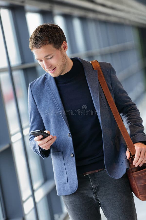 Man on smart phone - young business man texting in airport. Casual urban professional businessman using smartphone app smiling happy inside office building or airport. Man on smart phone - young business man texting in airport. Casual urban professional businessman using smartphone app smiling happy inside office building or airport.