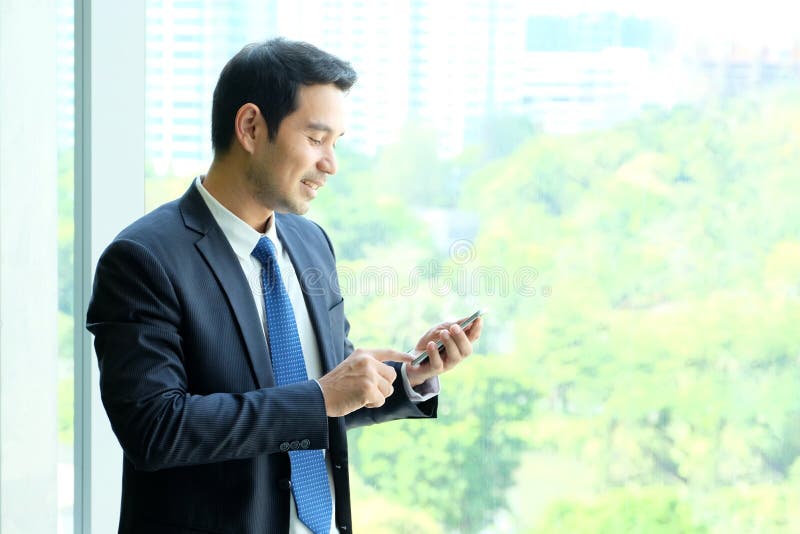 Business man using smart phone by windows with city view, inside