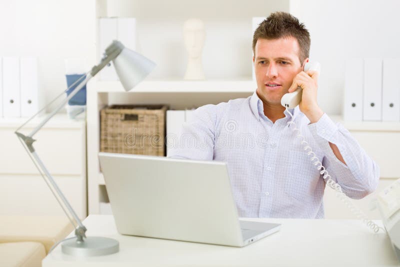 Business man working on computer at home calling on phone. Business man working on computer at home calling on phone.