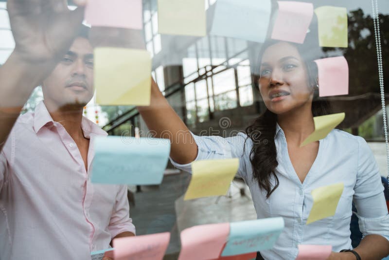 Business partner brainstorming by sticking idea into the glass window stock photo Business partner brainstorming by sticking idea into the glass window stock photo