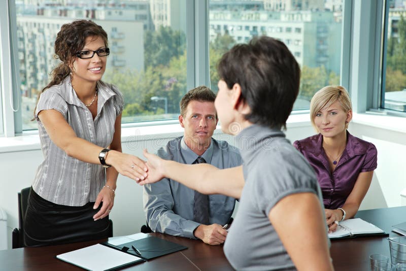 Pannello di uomini d'affari, seduto al tavolo nella sala riunioni di conduzione di un colloquio di lavoro saluto femminile richiedente.