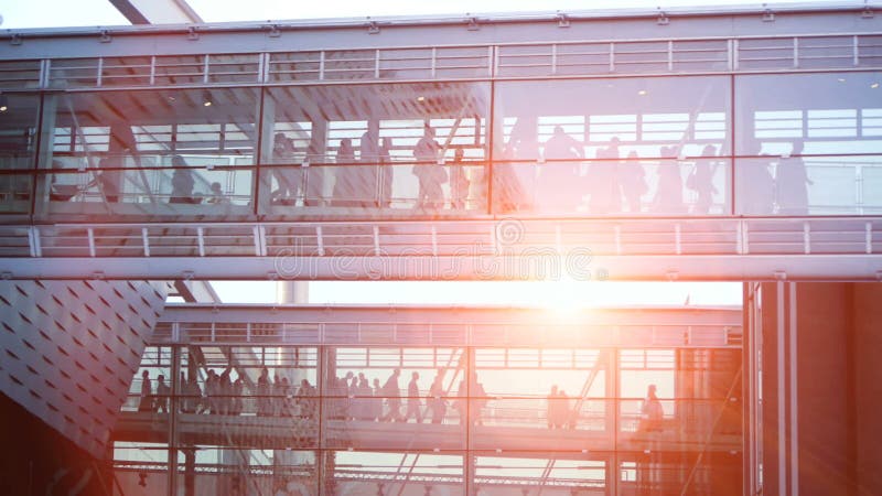 Business people waling trough modern glass corridor building. sunset sky