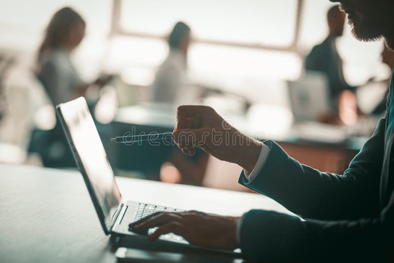 Business people working in open space office. Selective focus on busy man using laptop in foreground. Close up shot