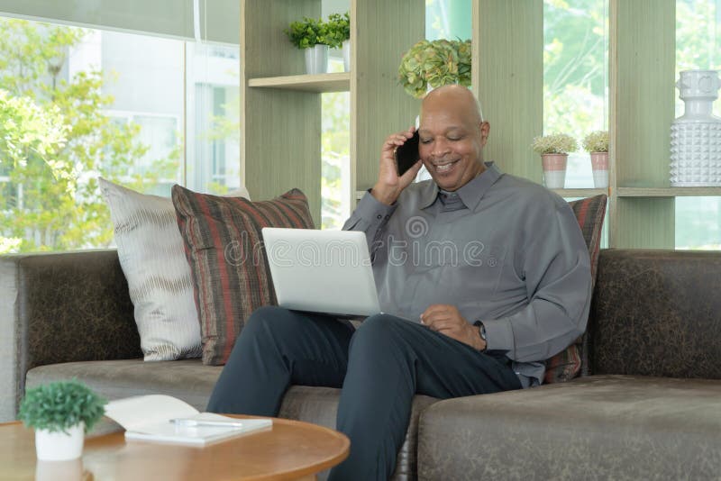 Business senior old elderly Black American man, African person using a smartphone or mobile phone in living room at home in