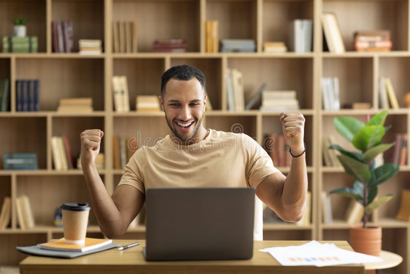 Business success. Overjoyed arab man using laptop and gesturing yes, shaking fists celebrating big luck stock photo