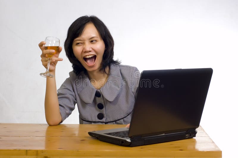 Beautiful asian business woman celebrating her success with wine in front of her computer