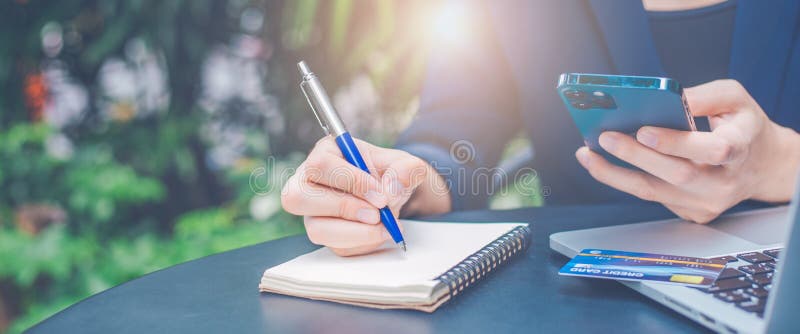 Business woman hand writing on a notepad with a pen and using laptop in the office. Web banner stock photo