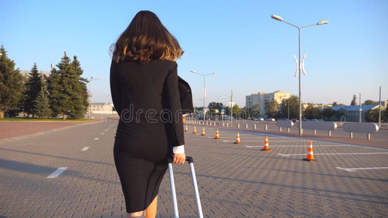 Business woman with her suitcase going from airport to taxi parking. Lady walking with her luggage along city street