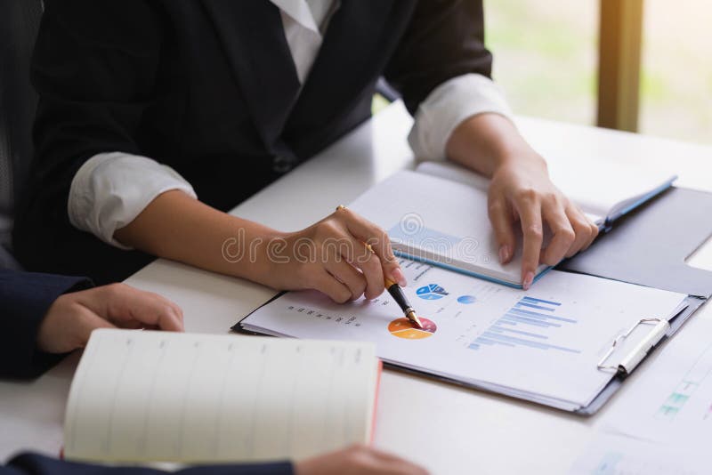 Business woman holding a pen pointing the graph and partnership to analyze the marketing plan with calculator on wooden table in stock photos Business woman holding a pen pointing the graph and partnership to analyze the marketing plan with calculator on wooden table in stock photos