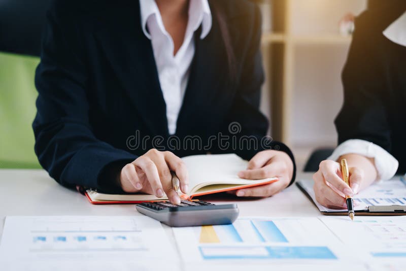 Business woman holding a pen pointing the report and partnership to analyze the marketing plan with calculator on wooden table in royalty free stock image Business woman holding a pen pointing the report and partnership to analyze the marketing plan with calculator on wooden table in royalty free stock image