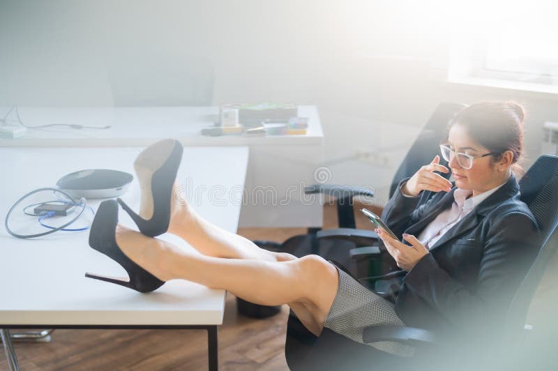 Business woman put feet on work desk and uses mobile phone in office.