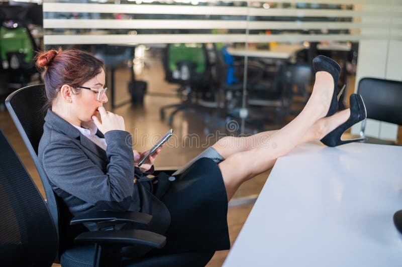 Business woman put feet on work desk and uses mobile phone in office.