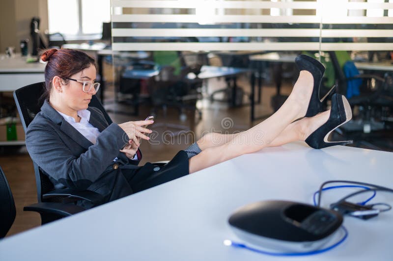 Business woman put feet on work desk and uses mobile phone in office.