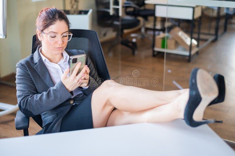 Business woman put feet on work desk and uses mobile phone in office.