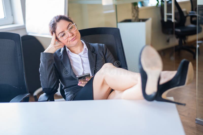 Business woman put feet on work desk and uses mobile phone in office.