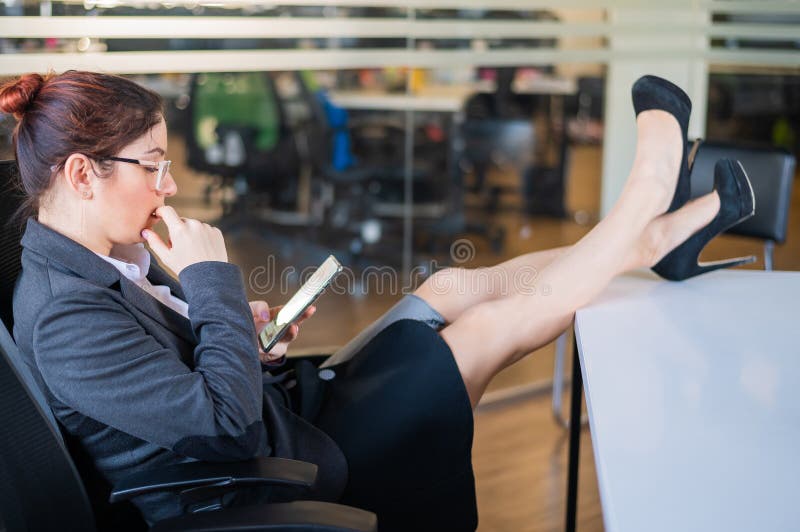 Business woman put feet on work desk and uses mobile phone in office.