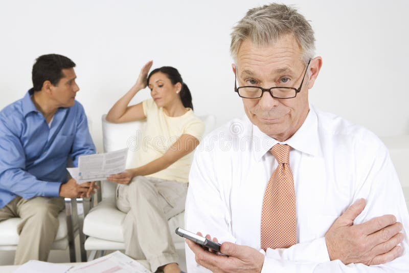 Senior financial advisor holding calculator with couple arguing in background. Senior financial advisor holding calculator with couple arguing in background