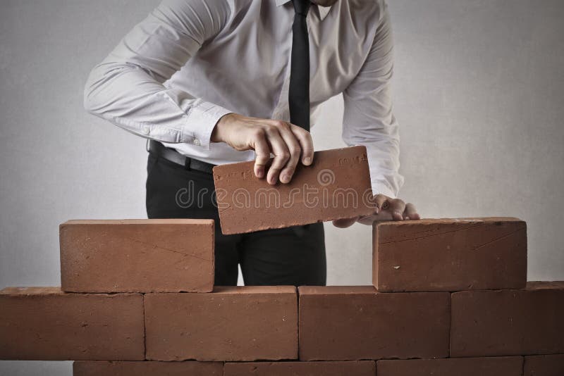 Businessman building a wall and putting a brick on it