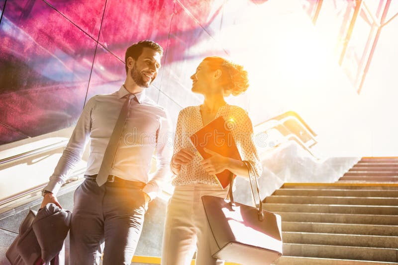 Businessman and businesswoman talking while walking down stairs with lens flare in background royalty free stock photo Businessman and businesswoman talking while walking down stairs with lens flare in background royalty free stock photo