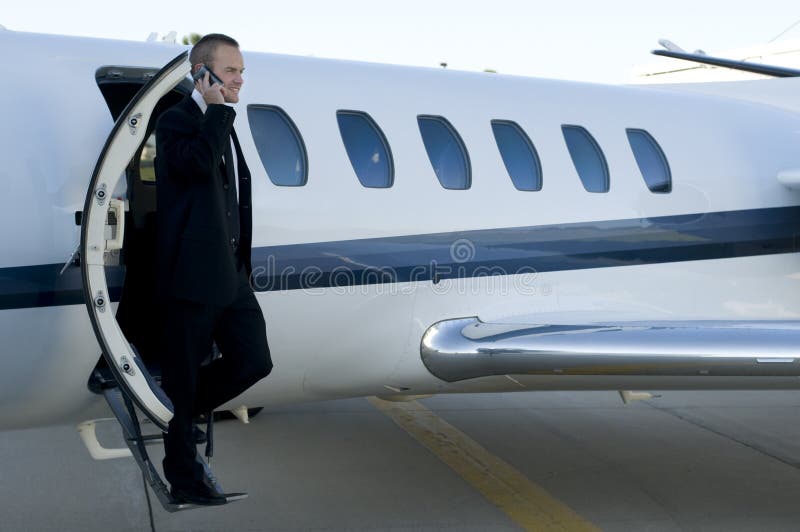 Businessman on cell phone exiting corporate jet. Young businessman talking on his cell phone as he leaves his corporate jet royalty free stock photography Businessman on cell phone exiting corporate jet. Young businessman talking on his cell phone as he leaves his corporate jet royalty free stock photography