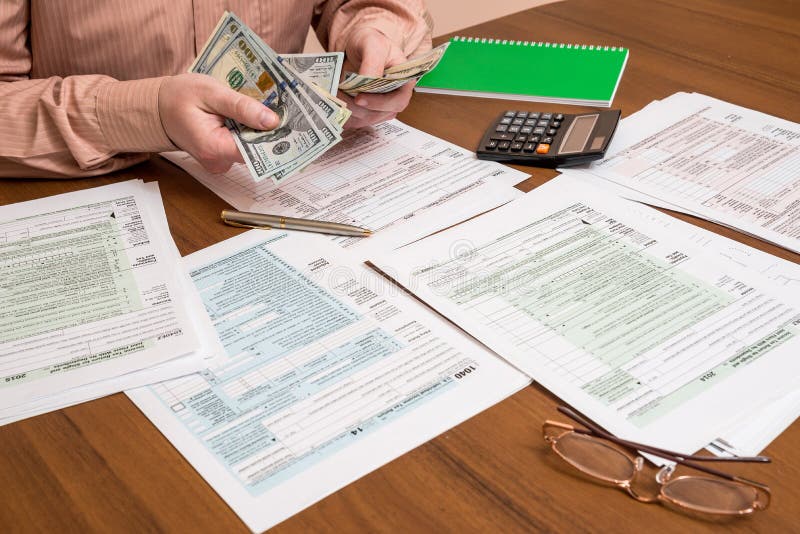 Businessman counting dollars on background of tax forms.