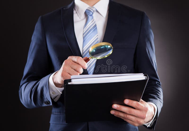 Midsection of businessman examining documents with magnifying glass against black background