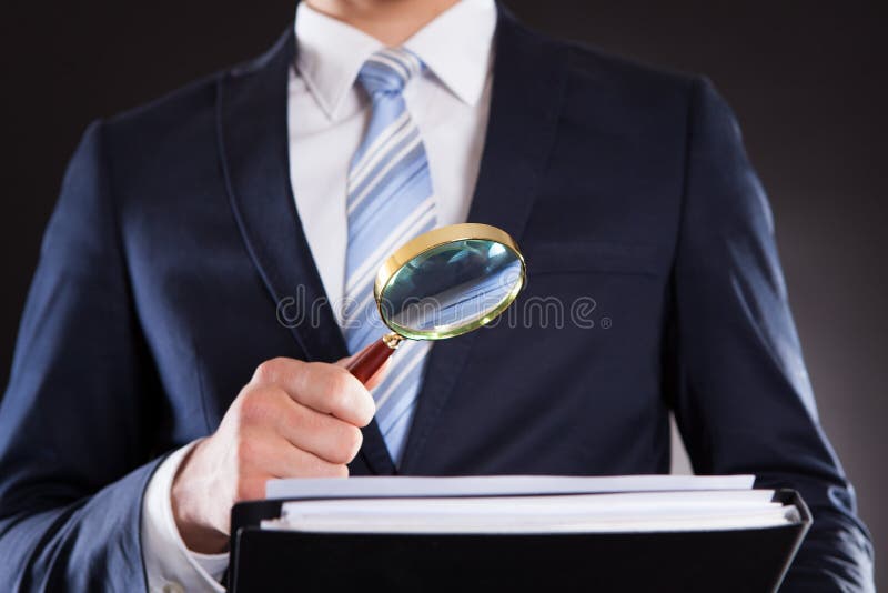 Midsection of businessman examining documents with magnifying glass against black background