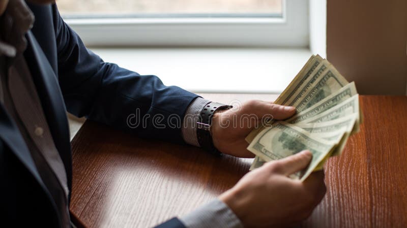 Businessman hand grabbing money, US dollar USD bills.man in suit. wood background