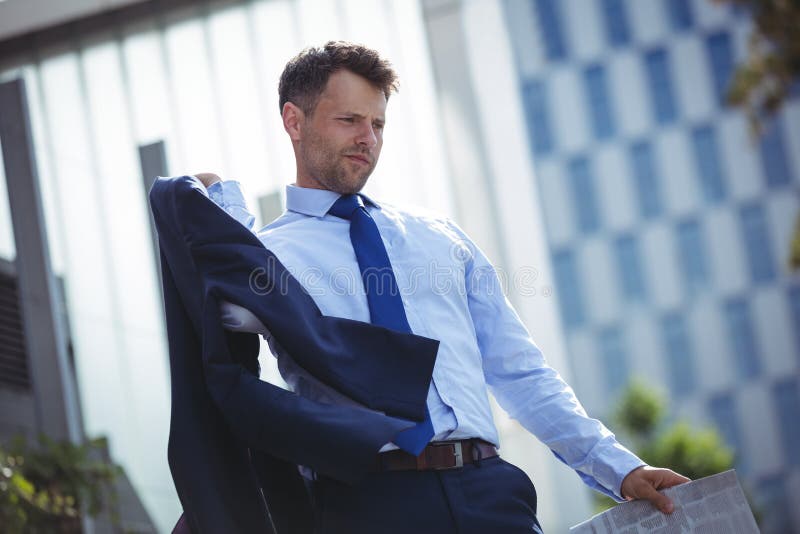 Businessman holding blazer and newspaper. Thoughtful businessman holding blazer and newspaper near office building royalty free stock photos Businessman holding blazer and newspaper. Thoughtful businessman holding blazer and newspaper near office building royalty free stock photos