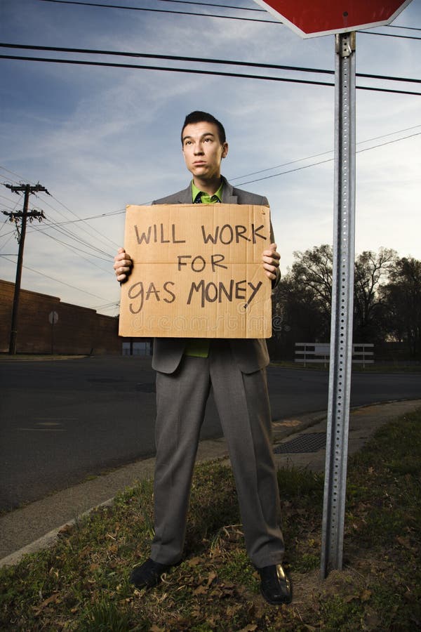 Young businessman stands on a street corner holding a sign that reads 'will work for gas money'. Vertical shot. Young businessman stands on a street corner holding a sign that reads 'will work for gas money'. Vertical shot.