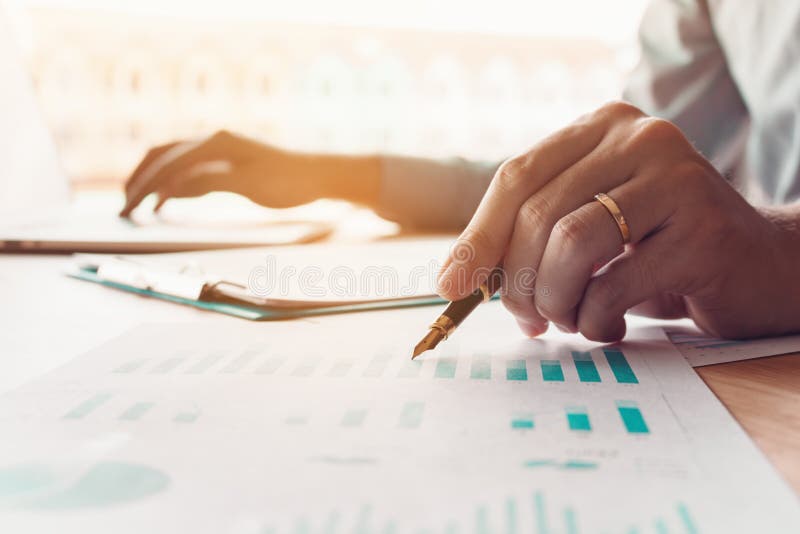 Businessman holding pen and pointing chart report paper on desk stock photos Businessman holding pen and pointing chart report paper on desk stock photos