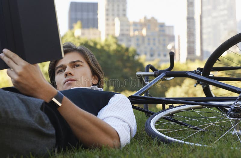 Businessman Lying Down on Bicycle while Reading Book Stock Image