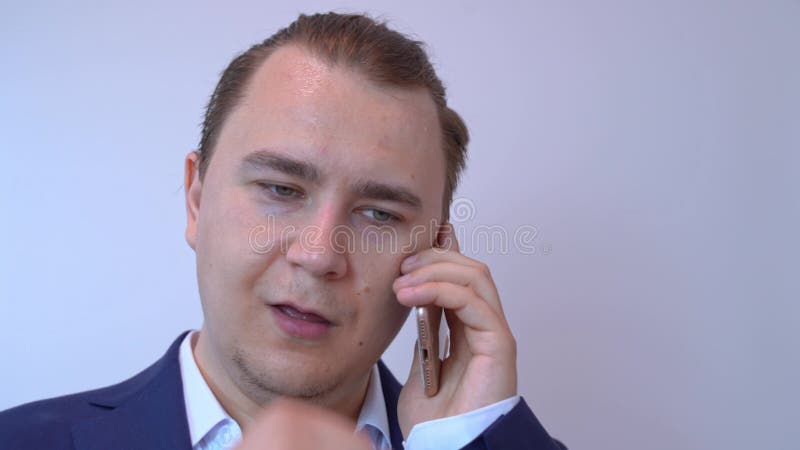 Businessman in a navy suit speaking on a smartphone with a focused expression against a plain background, coughs