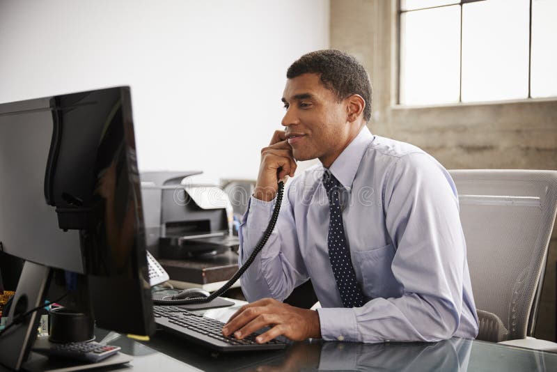 Businessman at an office desk using phone and computer