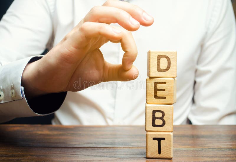 Businessman removes wooden blocks with the word Debt. Reduction or restructuring of debt. Bankruptcy announcement. Refusal to pay stock images Businessman removes wooden blocks with the word Debt. Reduction or restructuring of debt. Bankruptcy announcement. Refusal to pay stock images