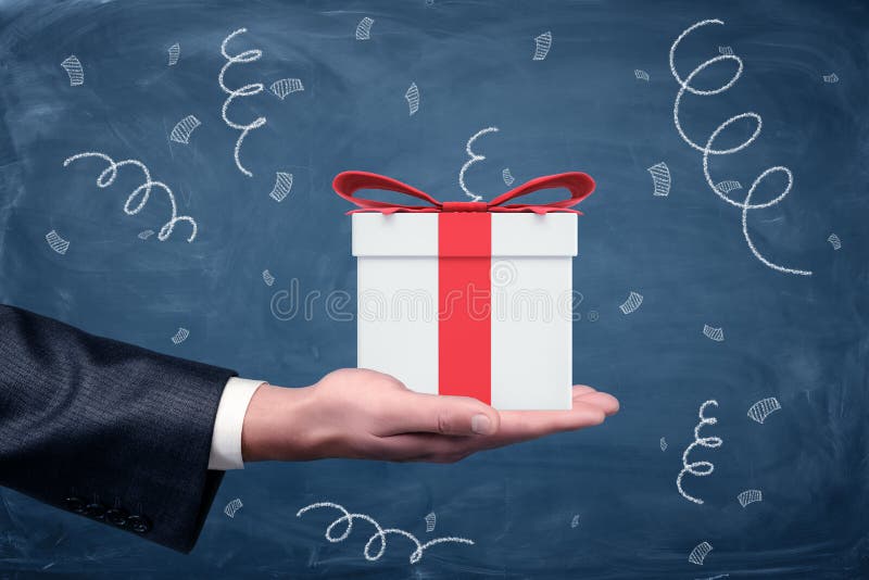 A businessman`s hand turned up and a small gift box with a red bow standing on chalkboard background.