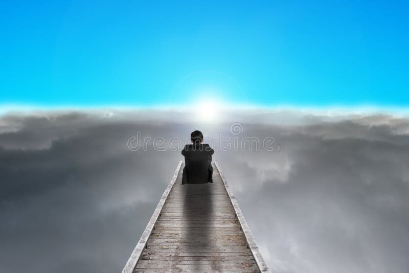 Businessman sitting on pier looking sunrise with clouds, blue sk