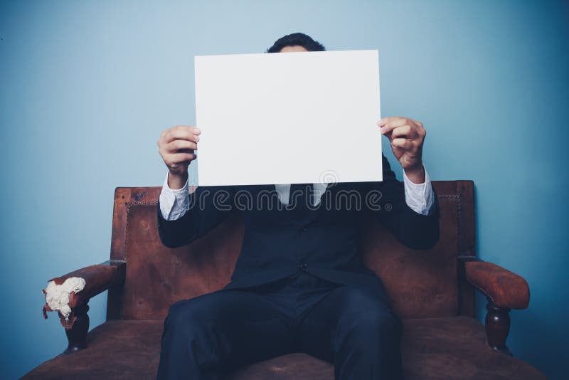 Businessman sitting on sofa holding blank white sign