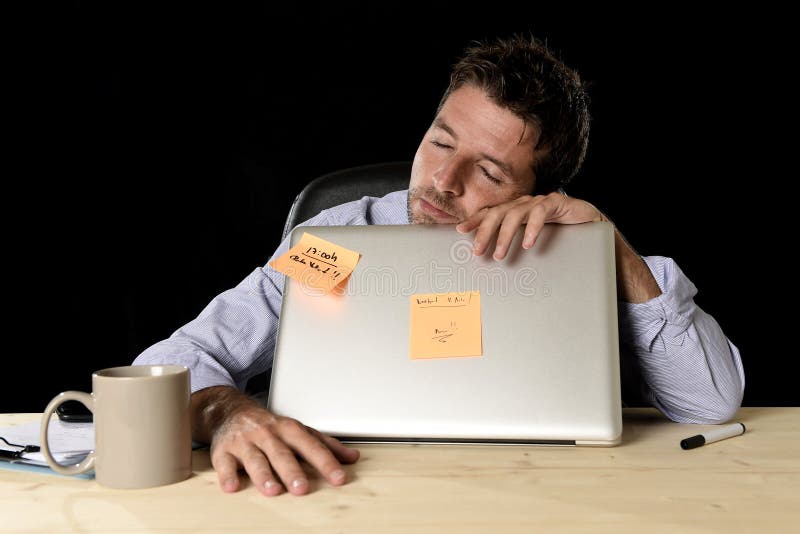 Young attractive businessman sleeping wasted and tired at office computer desk in long hours of work late at night and business stress concept in black background. Young attractive businessman sleeping wasted and tired at office computer desk in long hours of work late at night and business stress concept in black background