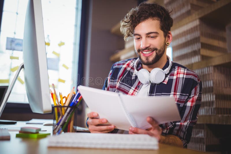 Businessman smiling while looking in book at computer desk