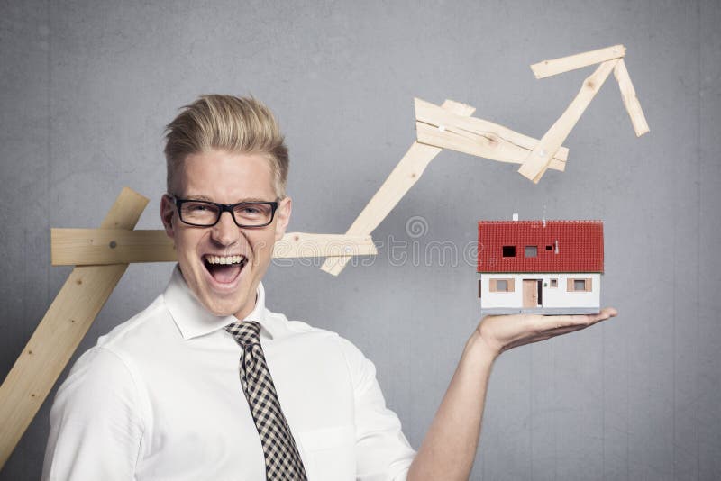 Concept: Success in real estate market. Happy businessman holding model house in hand in front of ascending business graph, isolated on grey background. Male hand holding businessman stock images, royalty-free photos and pictures