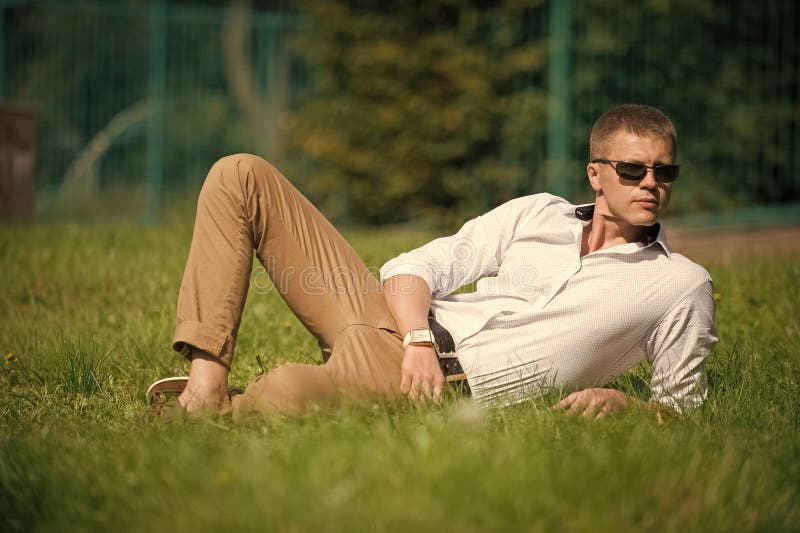 Businessman in sunglasses on sunny outdoor. Man relax on green grass. Handsome macho enjoy summer day. Fashion style and stock image Businessman in sunglasses on sunny outdoor. Man relax on green grass. Handsome macho enjoy summer day. Fashion style and stock image