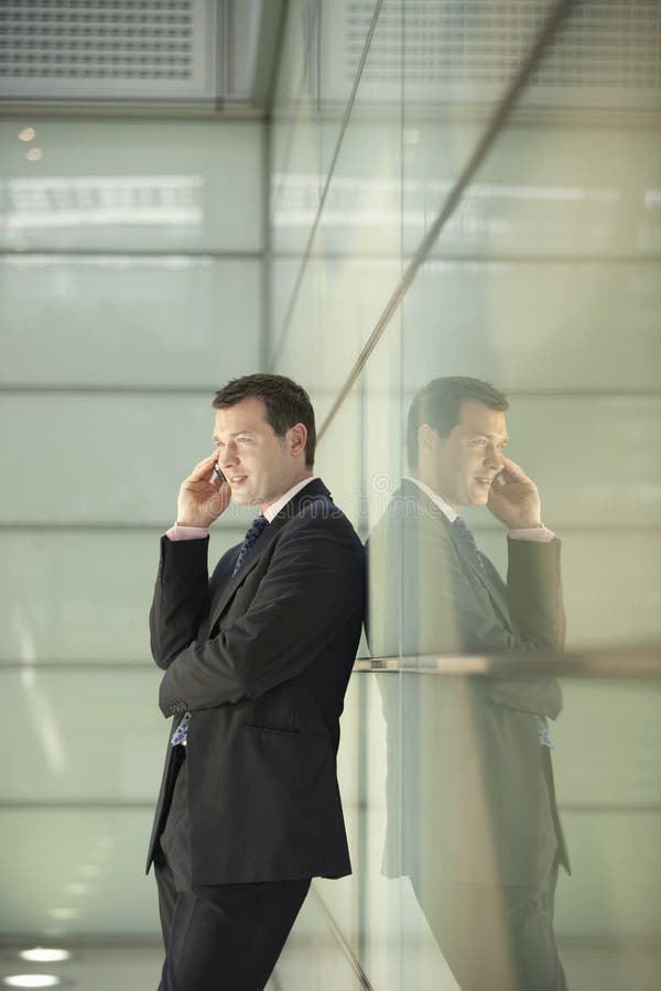 Businessman Using Cellphone While Leaning On Glass Wall