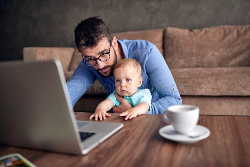 Businessman using a laptop computer for work at home while looking after his baby son.