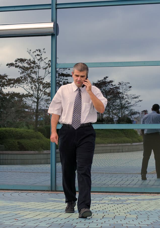 Businessman using mobile phone while is walking in hurry in front of a blue corporate building.