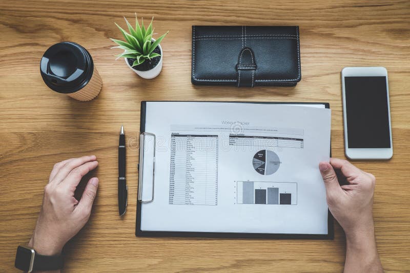 Businessman working on a graph document financial report and analysis calculation cost with calculator at office desk and other objects around, Top view workspace